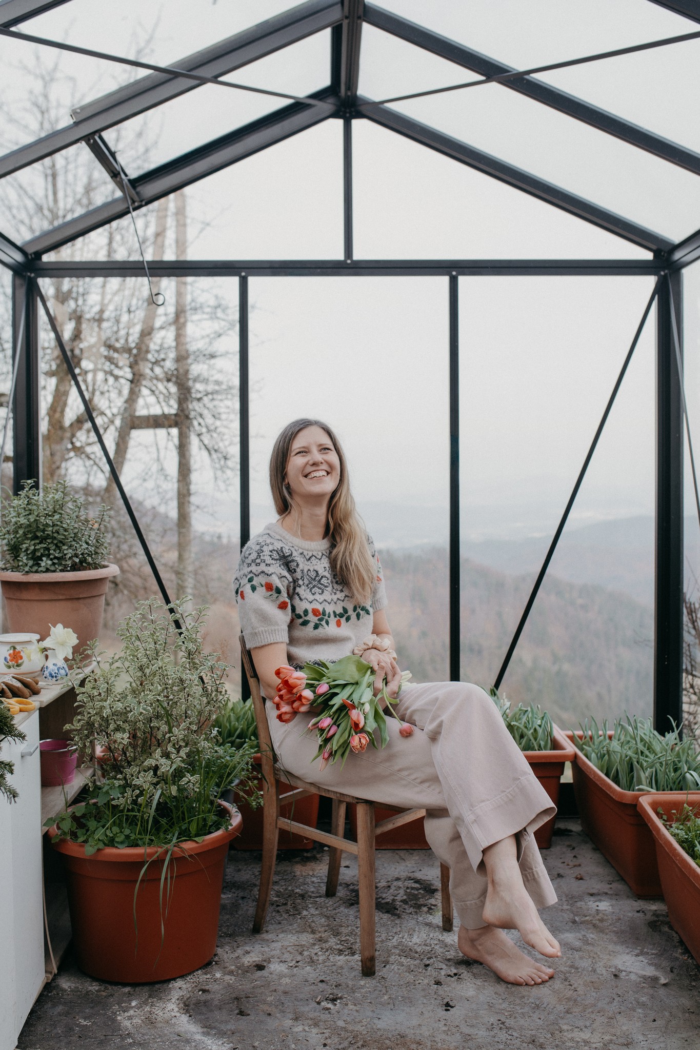 A smiling woman sitting in her greenhouse, holding a bouquet of tulips